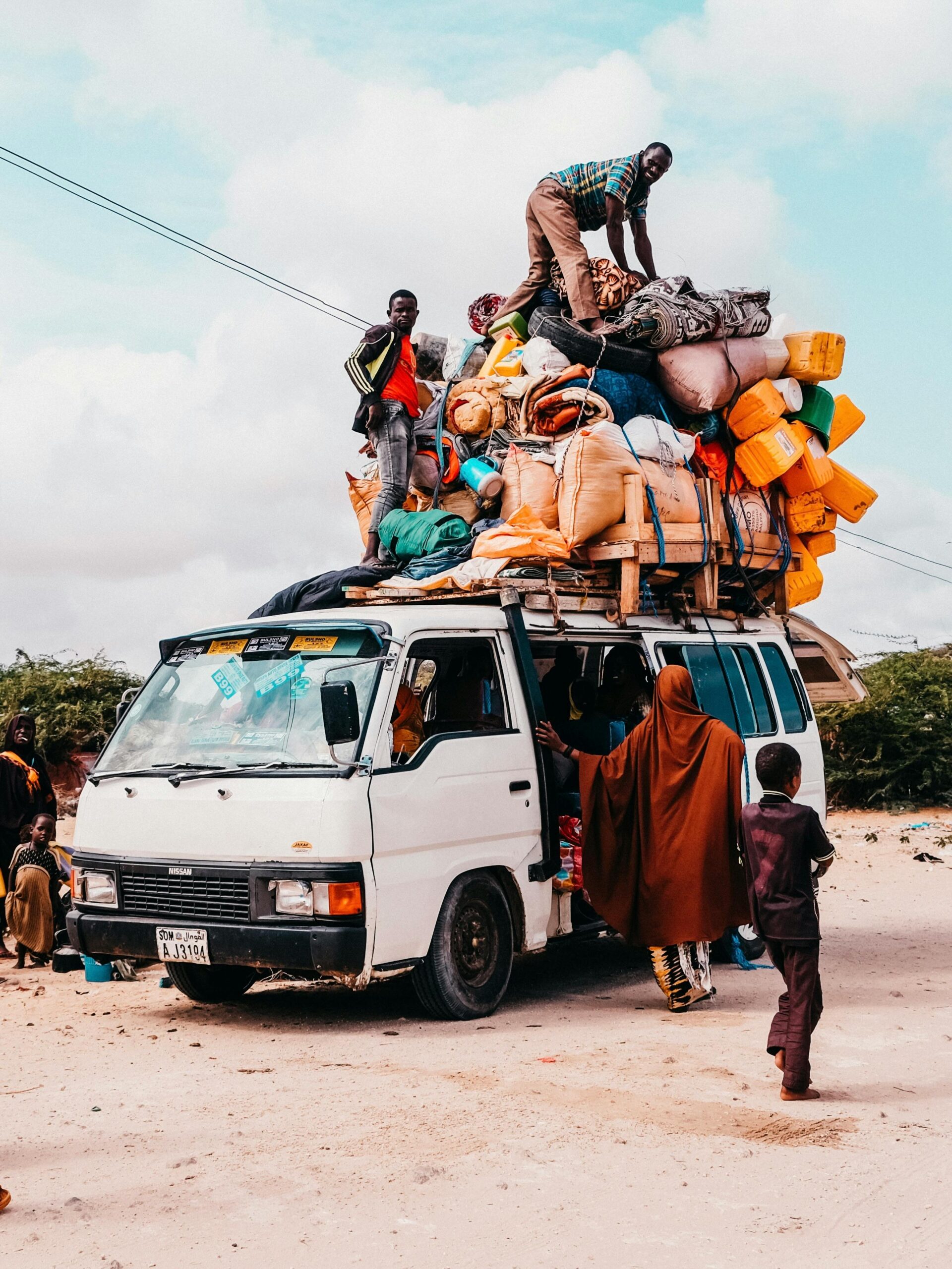 A crowded van carries people and luggage on a rural road, illustrating vibrant travel life.