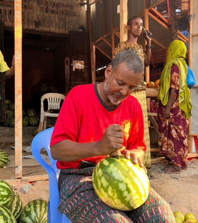 A vendor skillfully slices watermelon at an outdoor market in Mogadishu, Somalia.